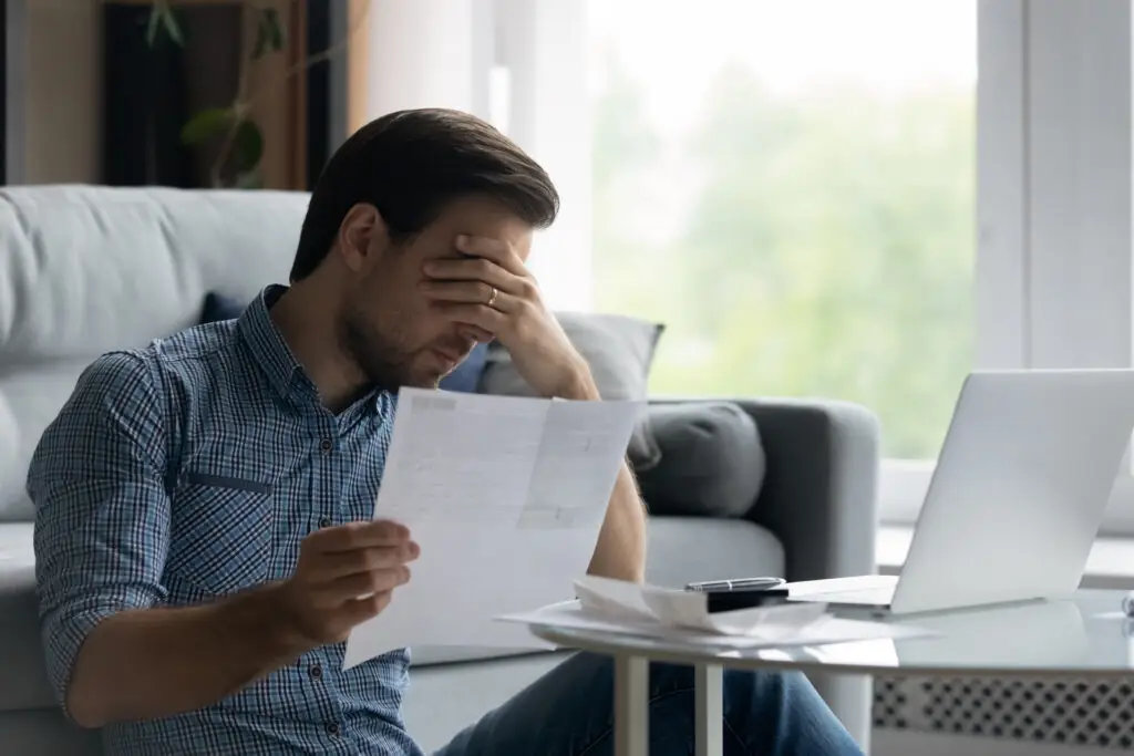Depressed unhappy young man covering eyes holding insurance document.
